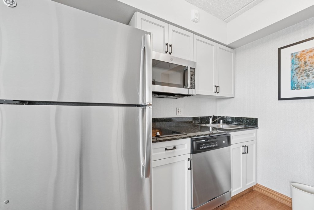 A white refrigerator is in a kitchen with white cabinets.