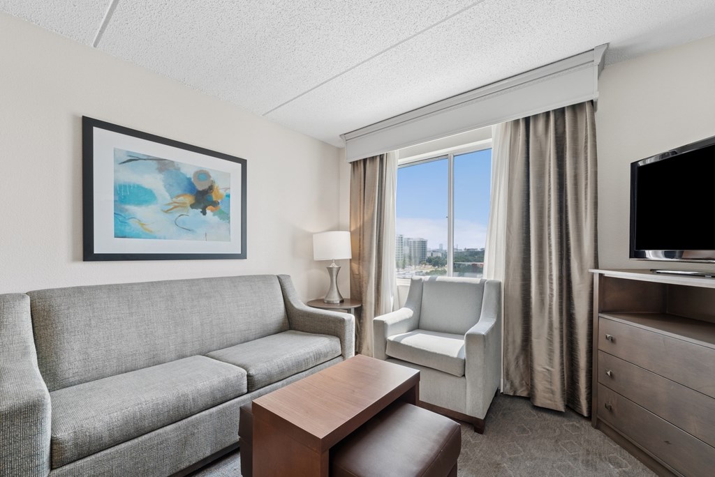 A living room with a grey couch, a brown coffee table, a white chair, a flat screen TV, and a painting on the wall.