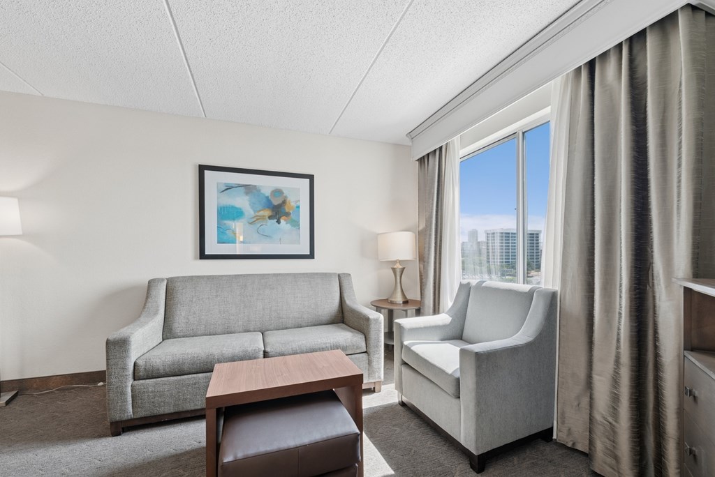 A living room with a grey couch, a white chair, and a painting on the wall.