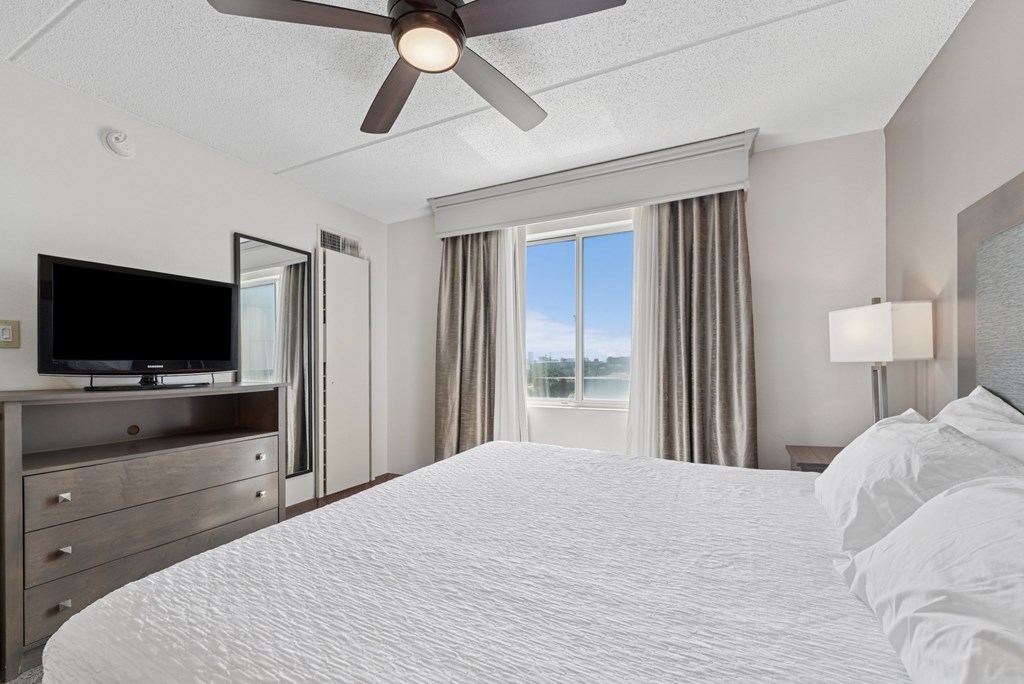 A bedroom with a large bed, a flat screen TV, and a sliding glass door leading to a balcony.