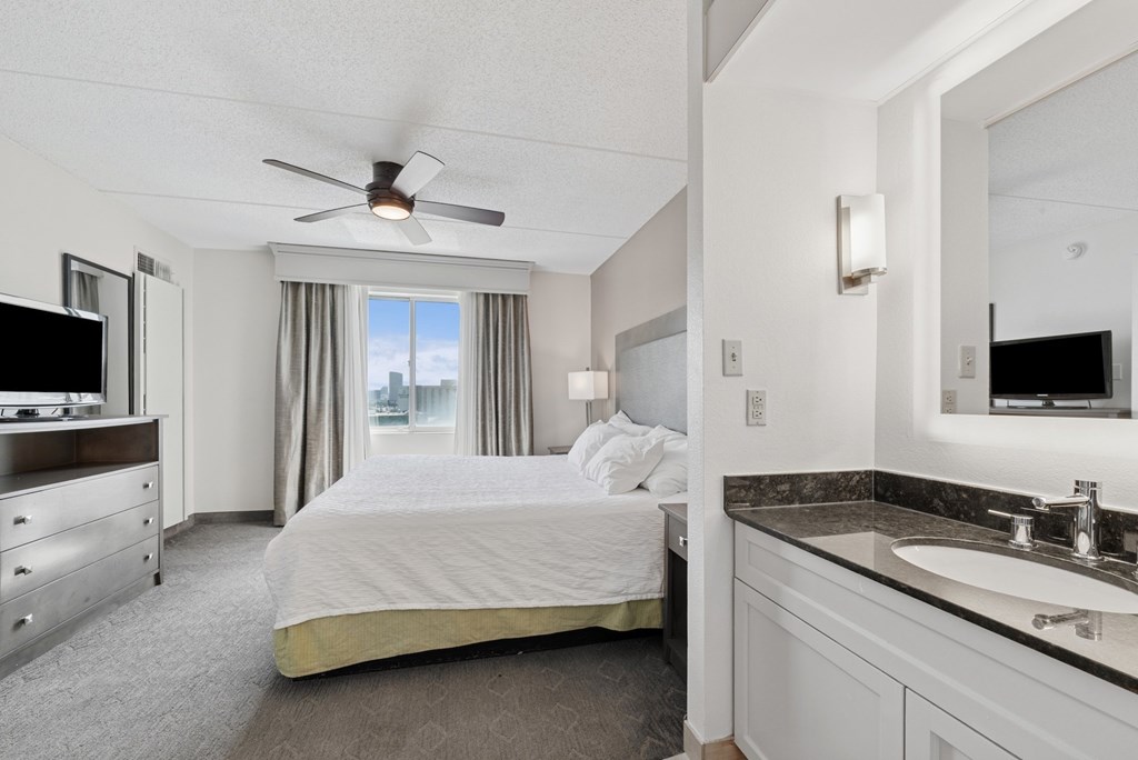 A well-lit, spacious hotel room with a large bed, a flat-screen TV, and a vanity area.