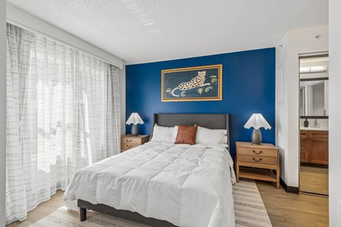 A bedroom with a large bed, a nightstand with a lamp, and a painting of a leaping animal on the wall.