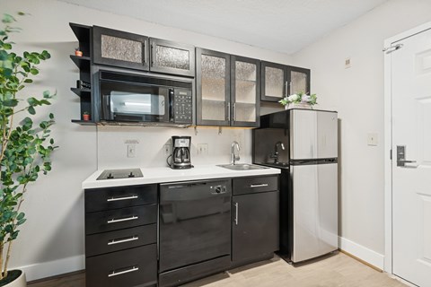 A kitchen with black cabinets and appliances, a white counter, and a door on the right.