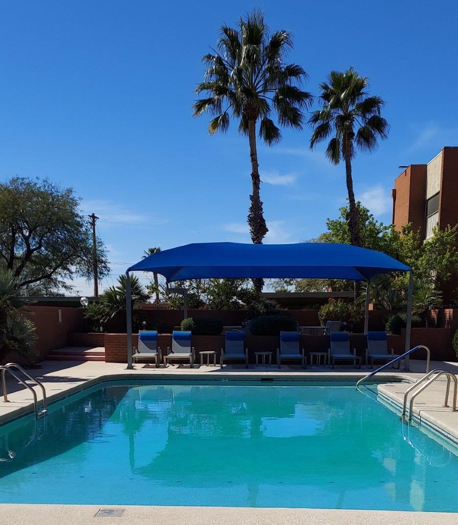 A pool with a blue umbrella and chairs under it.