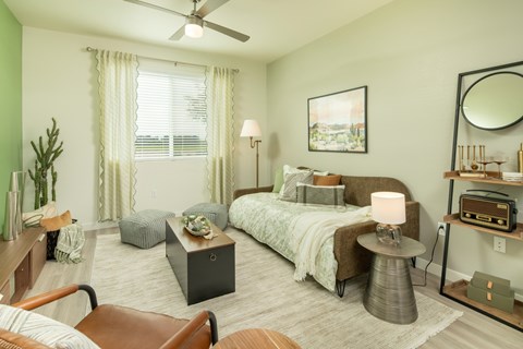 A bedroom with a bed, a chair, a table, and a ceiling fan.