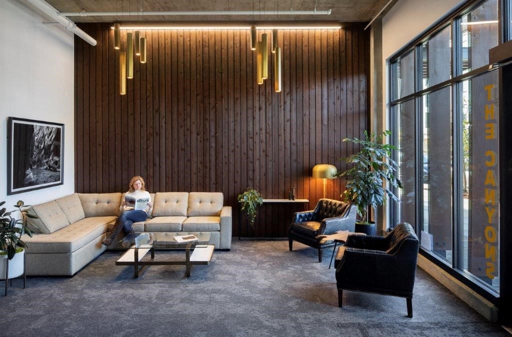 a woman sits on a couch in a living room with large windows
