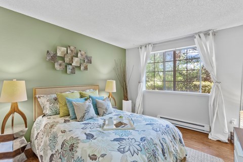 Bedroom with large window, wood-style flooring, and green accent wall at Cedar Crest Apartments in West Beaverton, Oregon.