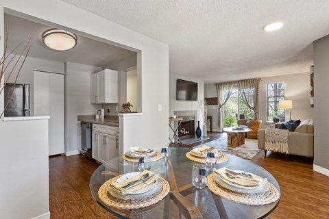 View of dining room, kitchen, and living room with white walls, fireplace, and wood-style flooring at Cedar Crest Apartments in West Beaverton, Oregon.