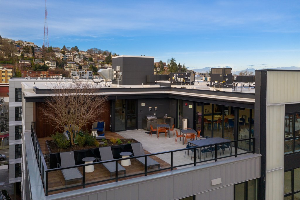 A rooftop patio with a table and chairs overlooks a cityscape.