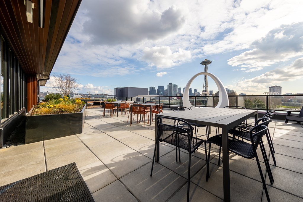 A table and chairs are set up on a patio with a city skyline in the background.