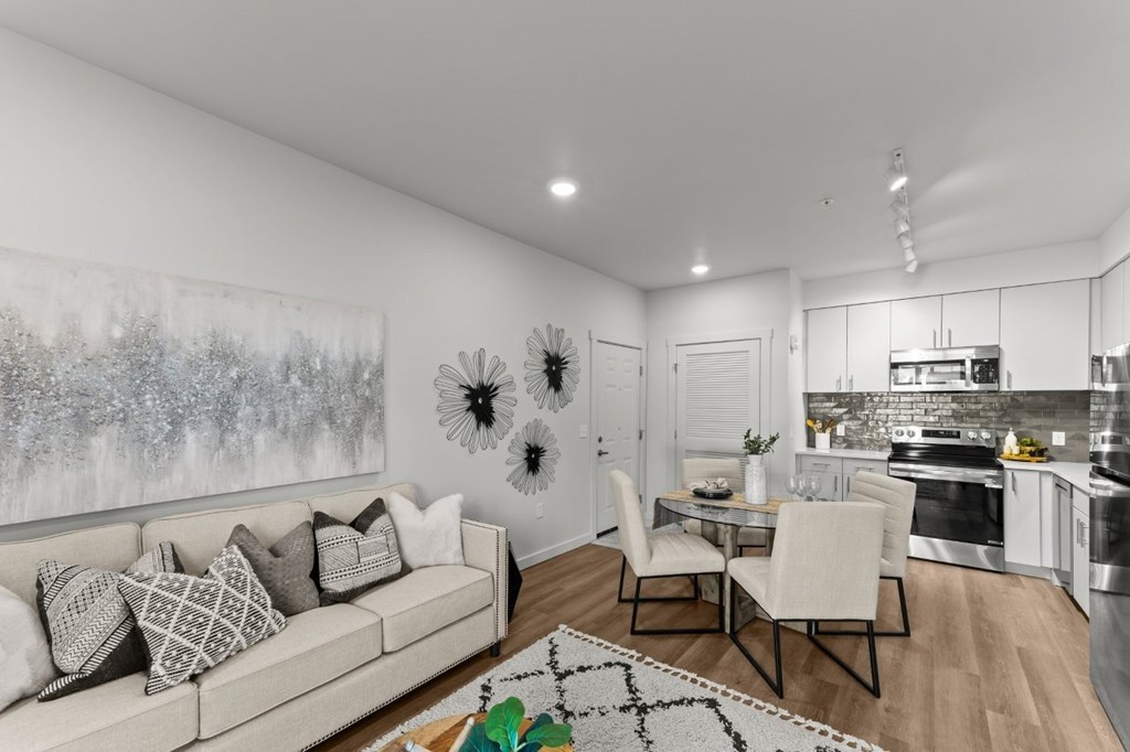 A modern living room with a large painting on the wall and a kitchen area in the background.