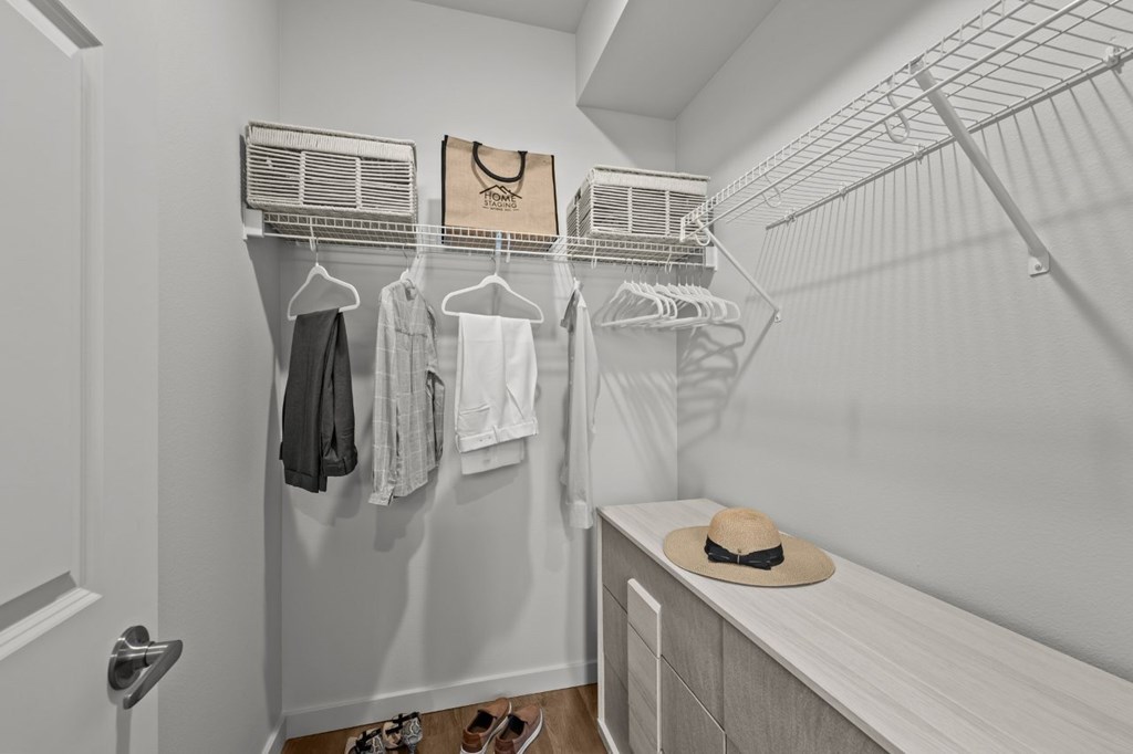 A closet with clothes hanging and a hat on a bench.