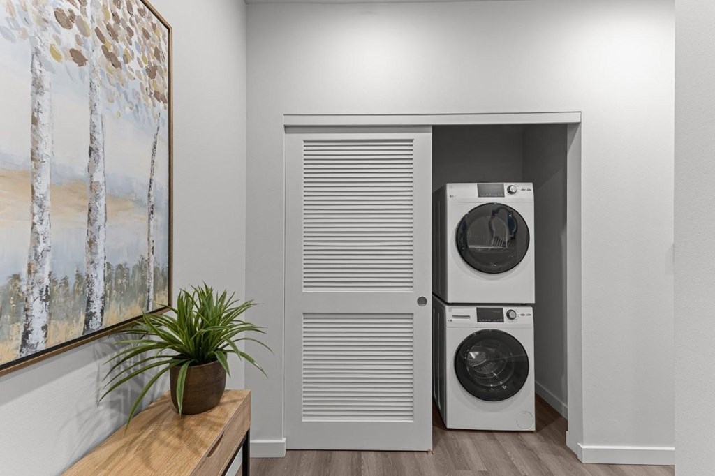 A room with a painting of trees on the wall and a washing machine in the doorway.