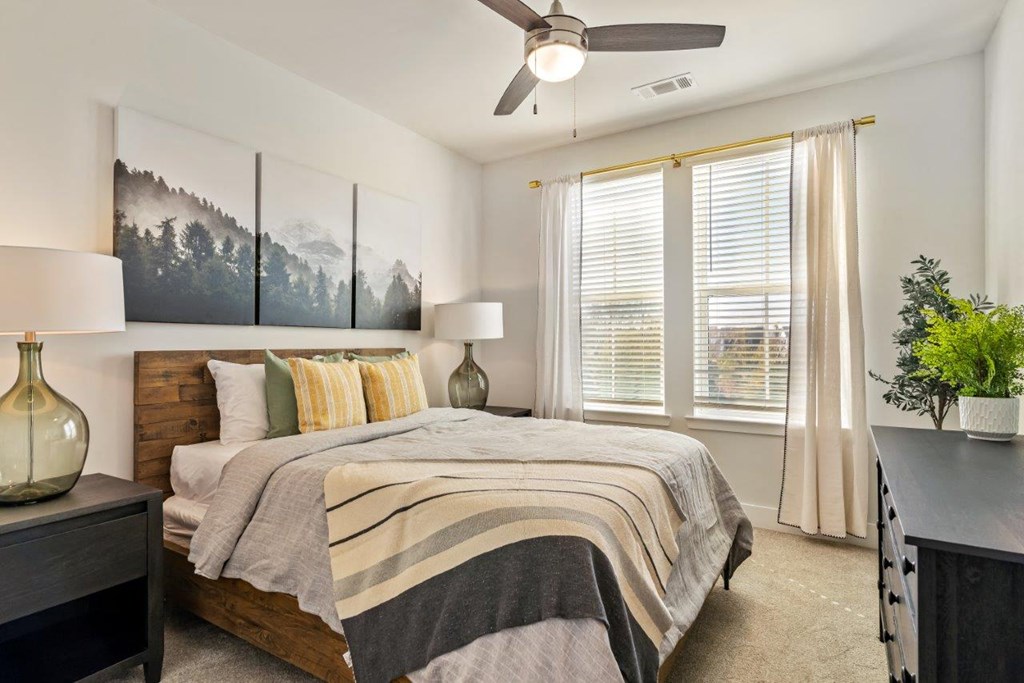 A bedroom with a bed, a ceiling fan, and a painting on the wall.