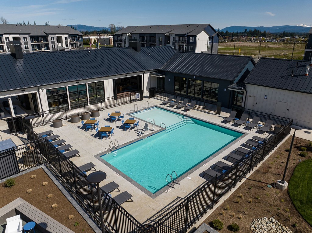 A large outdoor swimming pool surrounded by lounge chairs and a fence.