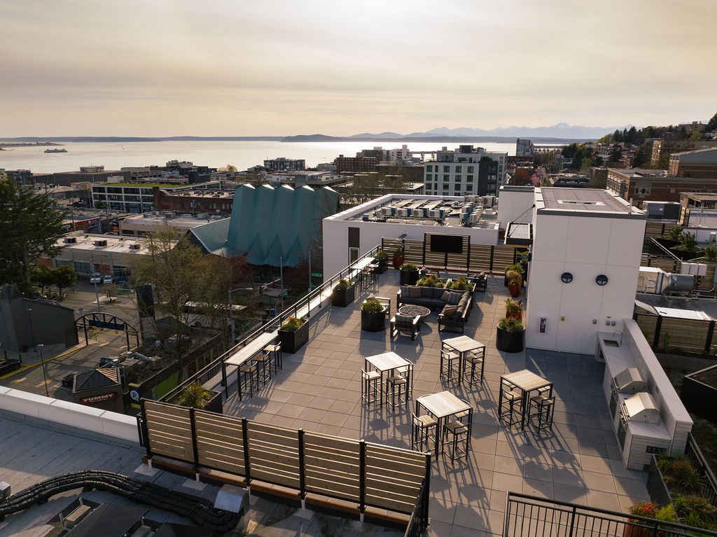 A rooftop patio with tables and chairs overlooks a cityscape.