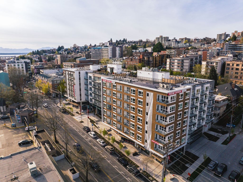 A large building with a red sign on the side is in the middle of a city street.