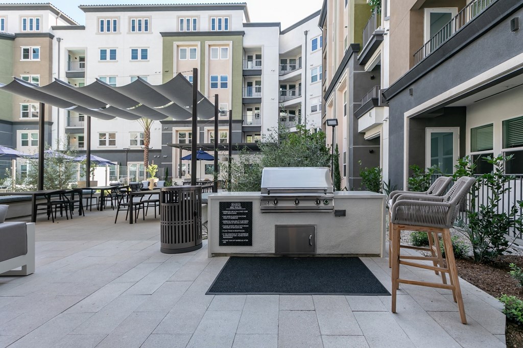 A patio with a grill and chairs is surrounded by apartment buildings.