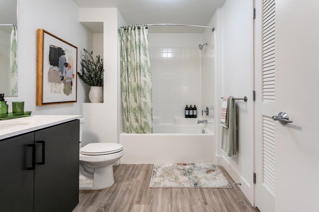 A bathroom with a toilet, a sink, a shower, and a rug.