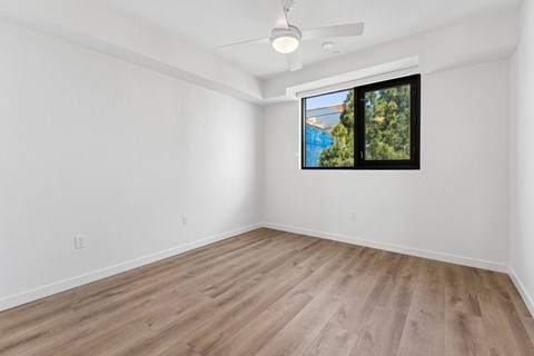 A room with a ceiling fan and a window overlooking a pool and trees.