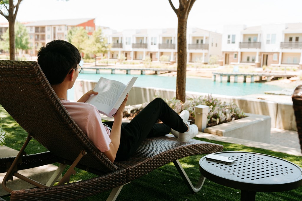 a woman sitting in a chair reading a book by a pool
