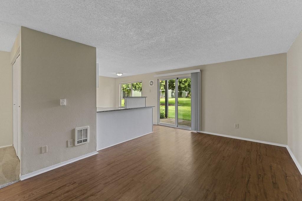 the living room and kitchen of an empty house with wood flooring and a door