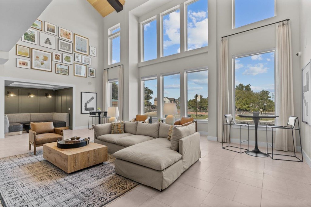A living room with a large couch, a coffee table, and a view of the trees outside the windows.