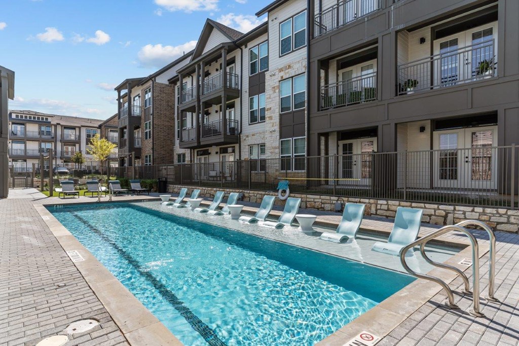 A pool with chairs around it in front of a building.