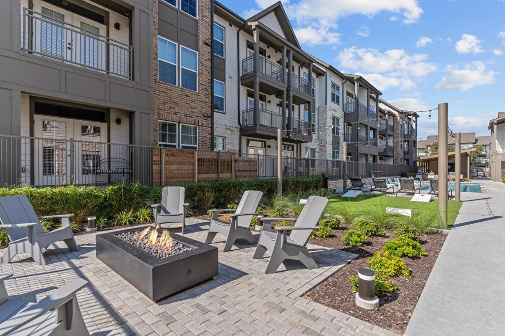 A modern outdoor seating area with a fire pit in the middle of a brick patio.