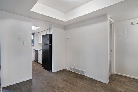 A black refrigerator sits in a kitchen with white walls and wood floors.