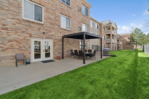 A patio with a black umbrella and chairs is in front of a brick building.