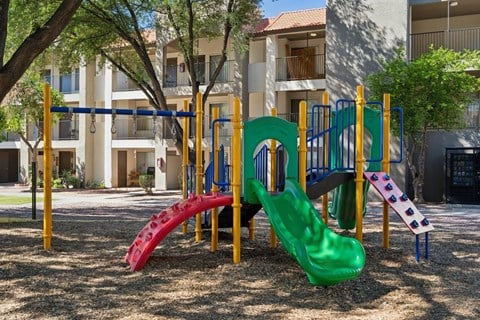 A playground with a green slide and a red slide in front of a building.