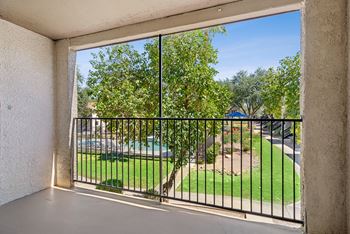 A balcony with a view of a green lawn and trees.