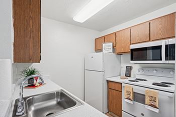 A kitchen with a white fridge, white stove, and a white sink.