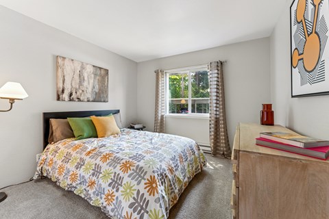 A bedroom with a bed, nightstand, and a painting on the wall.