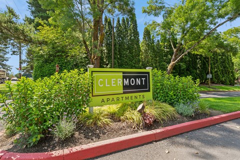 A sign for Clermont Apartments is surrounded by greenery.