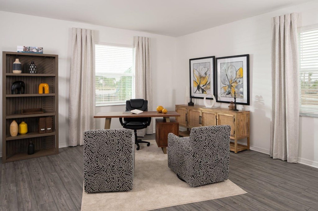 a living room with a desk and chairs and a window