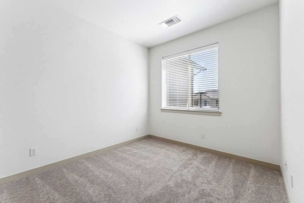 A room with a carpeted floor and a window with blinds.
