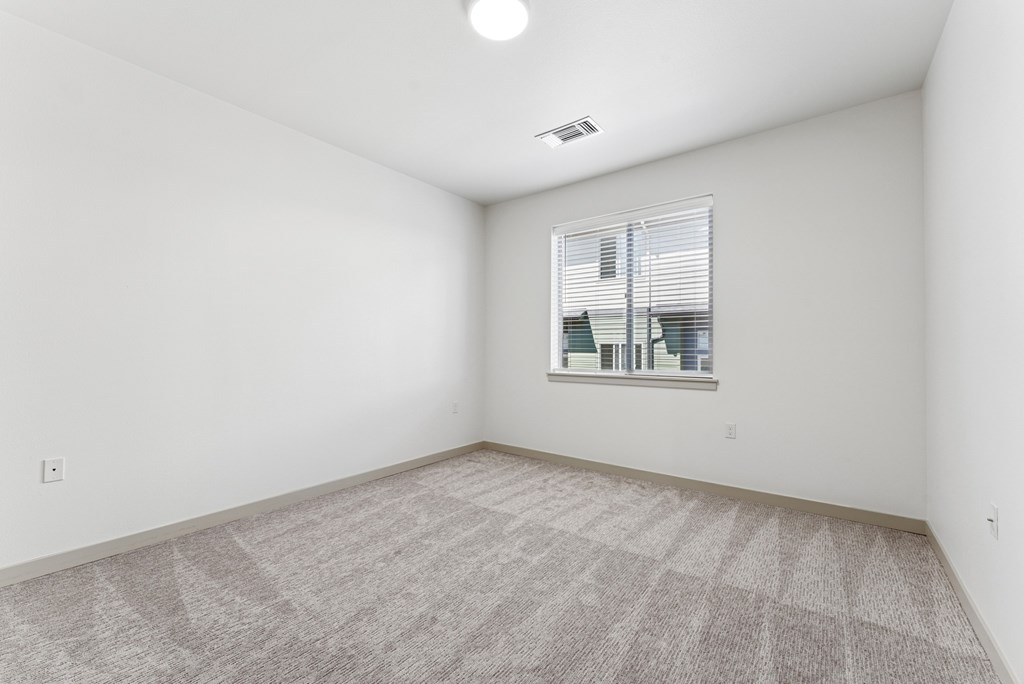 A room with a carpeted floor and a window with blinds.