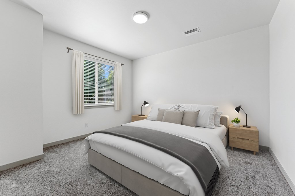 A bedroom with a large bed, nightstand, and window with blinds.