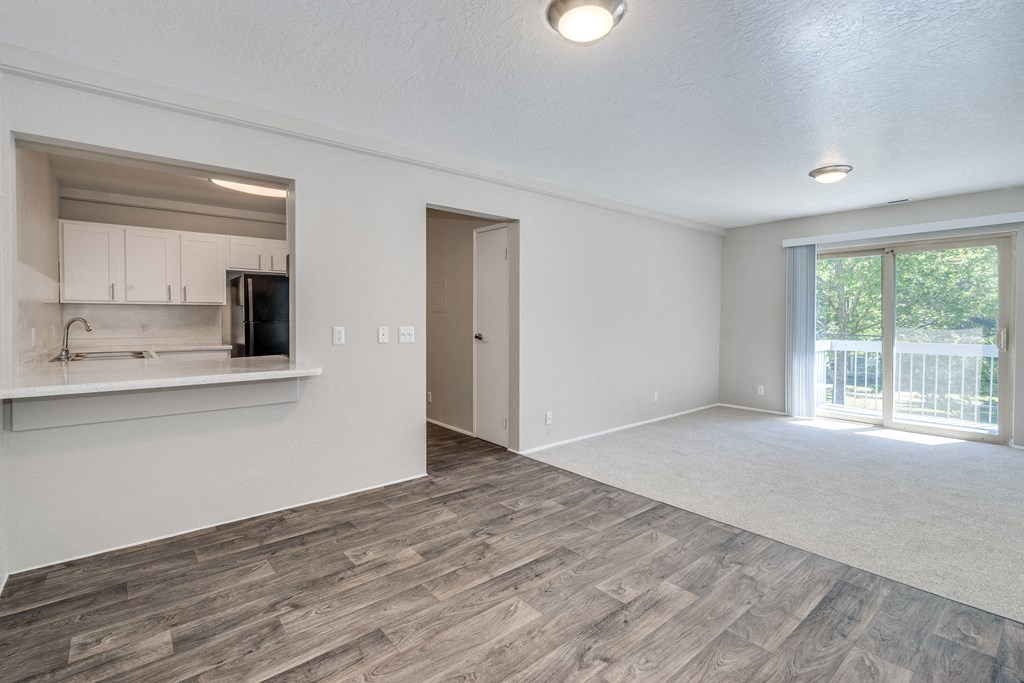 an empty living room and kitchen with a door to a balcony