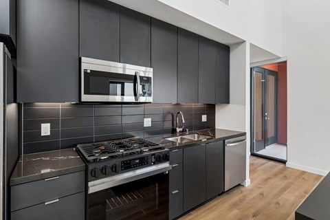 A modern kitchen with dark grey cabinets and a stainless steel stove top.