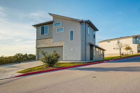 A modern two-story house with a garage is situated on a street with a red curb.