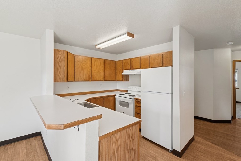 A white kitchen with wooden cabinets and a white fridge.