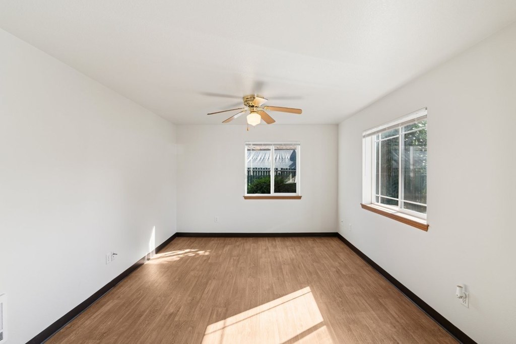 A room with a ceiling fan and two windows.