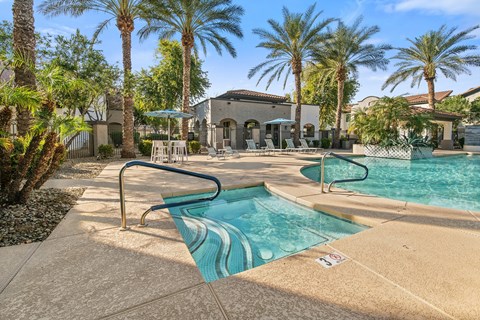 A pool surrounded by palm trees and a building in the background.