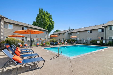 A pool area with sun loungers and umbrellas in front of apartment buildings.