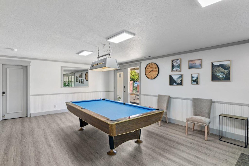 A pool table in a room with a clock and pictures on the wall.