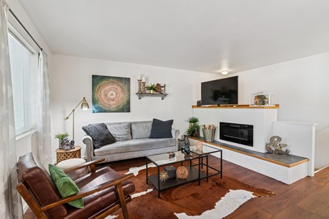 A living room with a grey couch, a brown leather chair, a glass coffee table, and a painting on the wall.