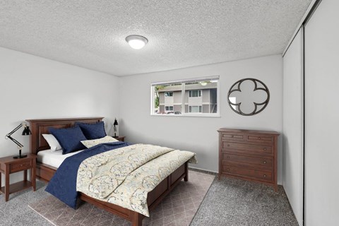 A bedroom with a bed, nightstand, and a window with a view of a building outside.